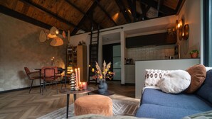 A cozy living room with a sofa, a coffee table, and a dining area with chairs. There is a kitchen visible in the background. - Fantastic luxury forest house | Unwind in nature (Emst)