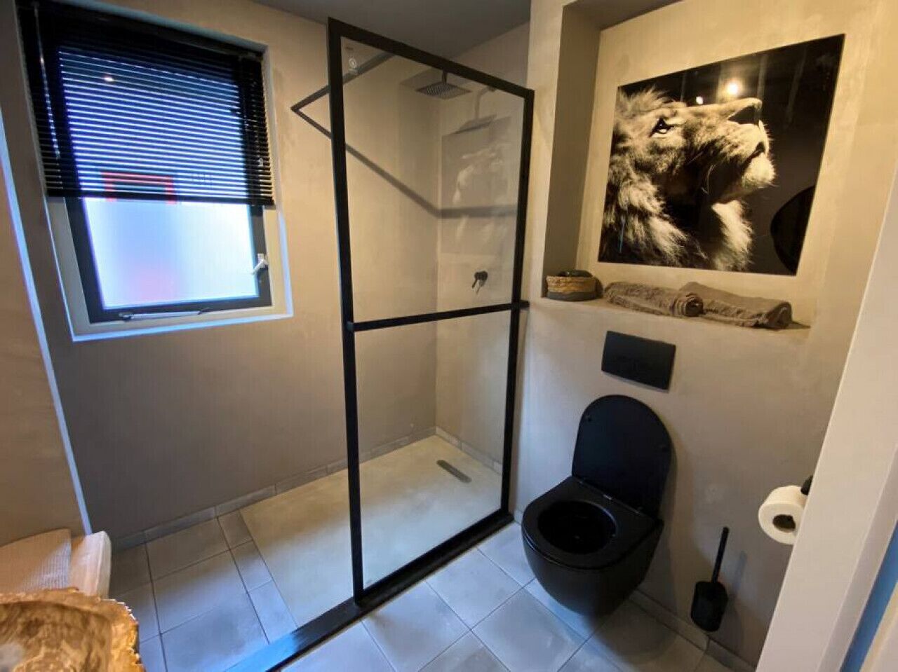 Een badkamer met een douchecabine van glas, een toilet en een raam met zonwering.
