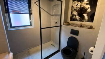 Een badkamer met een douchecabine van glas, een toilet en een raam met zonwering.