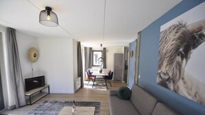 A modern living room with a sofa, a coffee table, and a TV. There is a dining area with a table and chairs in the background. - Comfortable wellness house, everything new, located by the lake. (Ewijk)