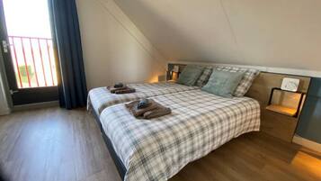 Quarto com teto inclinado, cama com colcha xadrez, duas almofadas e mesa de cabeceira com abajur.