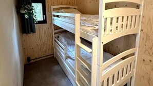Une pièce en bois avec des lits superposés, une fenêtre et une plante.