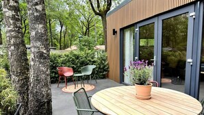 Une terrasse extérieure moderne avec une table ronde en bois, des chaises vertes et rouges, et une plante en pot.