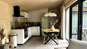 A modern kitchen with white cabinets, a black range hood, and a dining area with a wooden table and chairs. - VHNT76 · FIKA Luxury holiday home for 4 people at Veluwe (Hoenderloo)