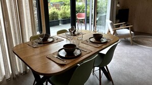 Un coin repas avec une table en bois dressée pour deux personnes, une vue sur la verdure à l’extérieur et un aménagement intérieur moderne.