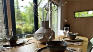 A dining table set with plates, bowls, and wine glasses, with a vase of dried plants on the table. - VHNT76 · FIKA Luxury holiday home for 4 people at Veluwe (Hoenderloo)