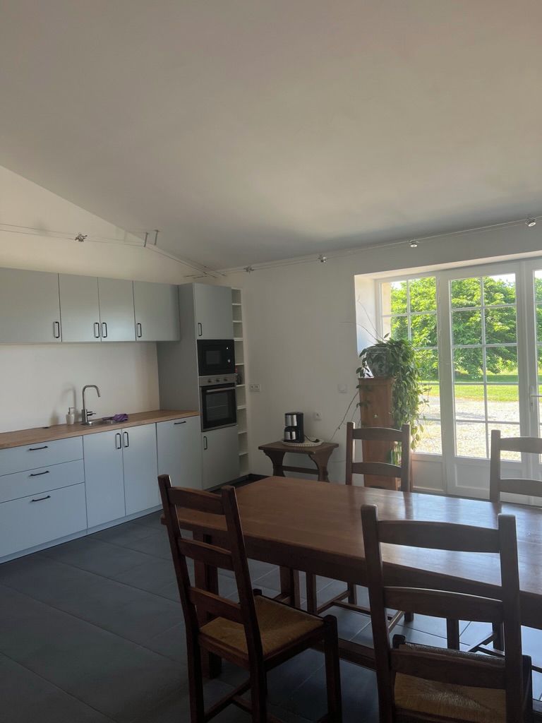 A modern kitchen with white cabinets, a dining table with chairs, and a view of greenery outside.