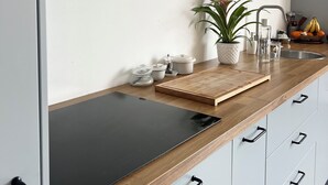 Moderni keittiö, jossa on musta työtaso, valkoiset kaapit, puinen leikkuulauta, ruukkukasvi ja hedelmäkulho.