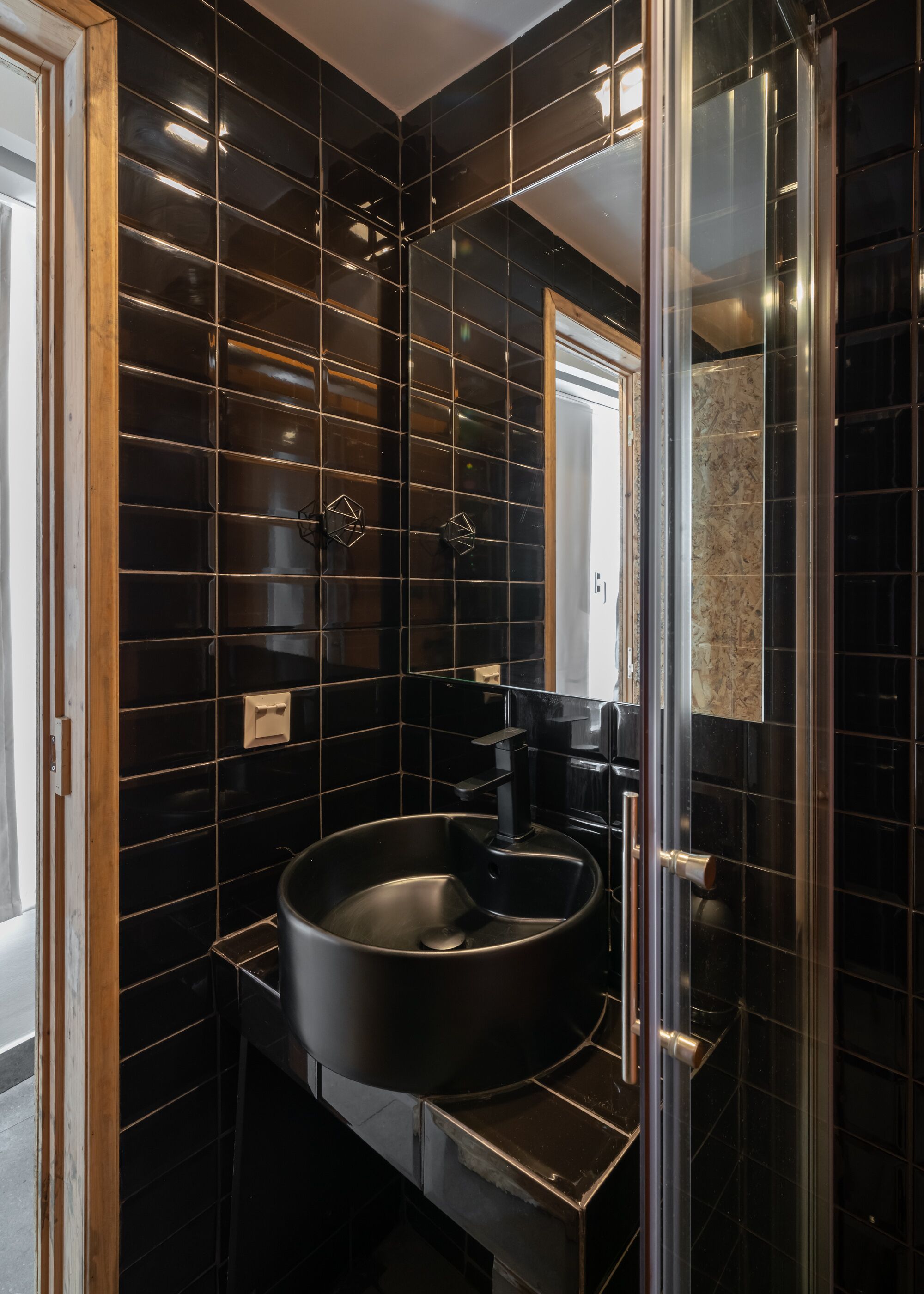 A modern bathroom with black tiled walls, a round sink, and a glass shower enclosure.