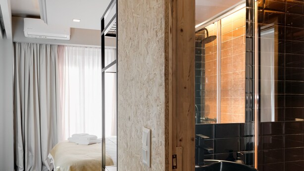 Quarto de hotel moderno com beliche, um espelho grande e banheiro com piso de azulejos pretos.