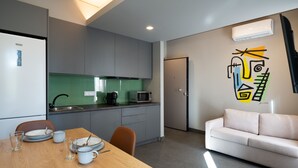 Uma cozinha moderna com armários cinza, um revestimento verde e um micro-ondas. Há uma mesa de jantar com pratos e copos, um sofá branco e uma parede com arte abstrata.