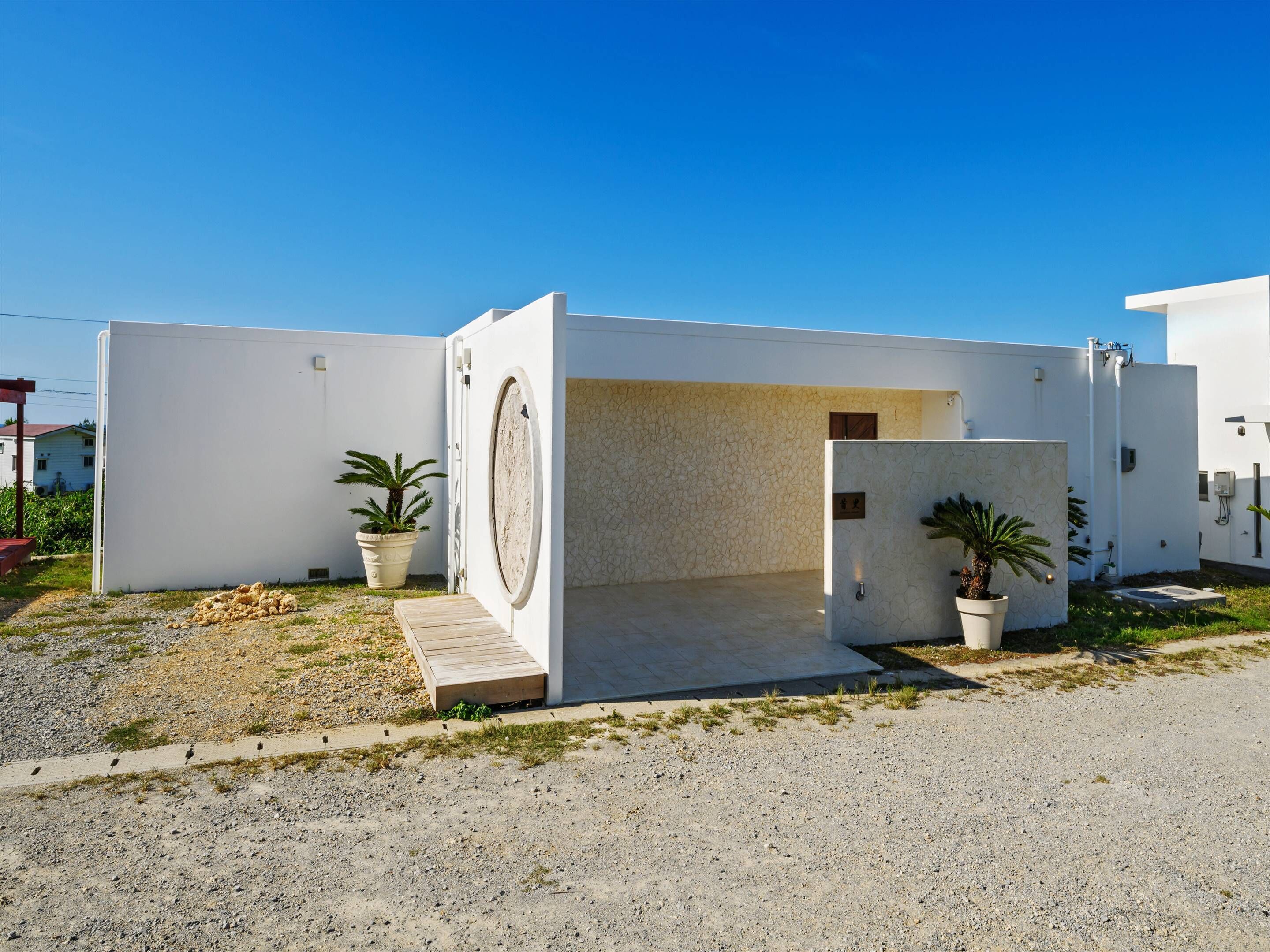 Un edificio moderno con un gran ventanal circular, una entrada pequeña y plantas en macetas.