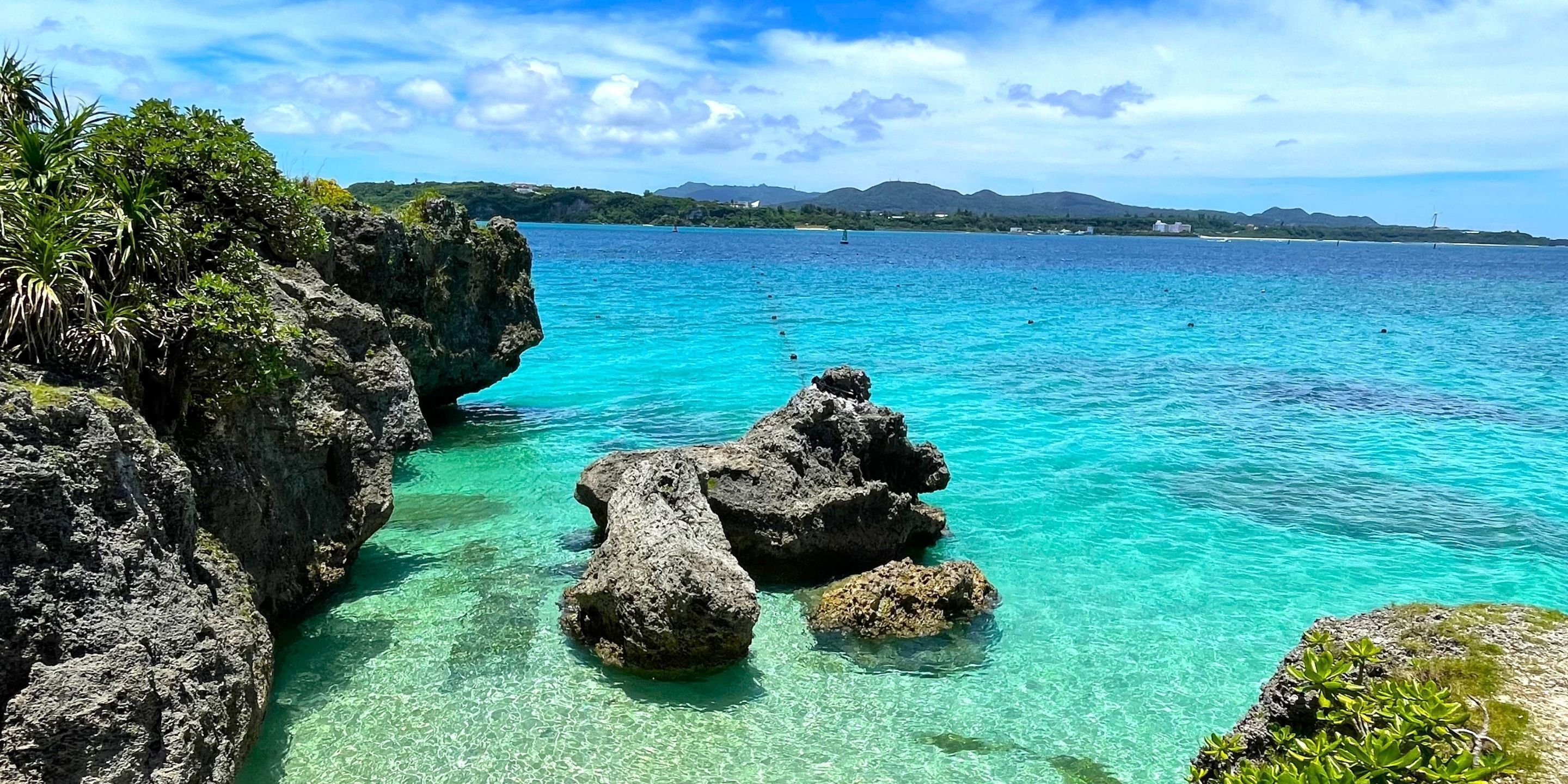 A coastal landscape with clear turquoise waters, rocky formations, and lush greenery.