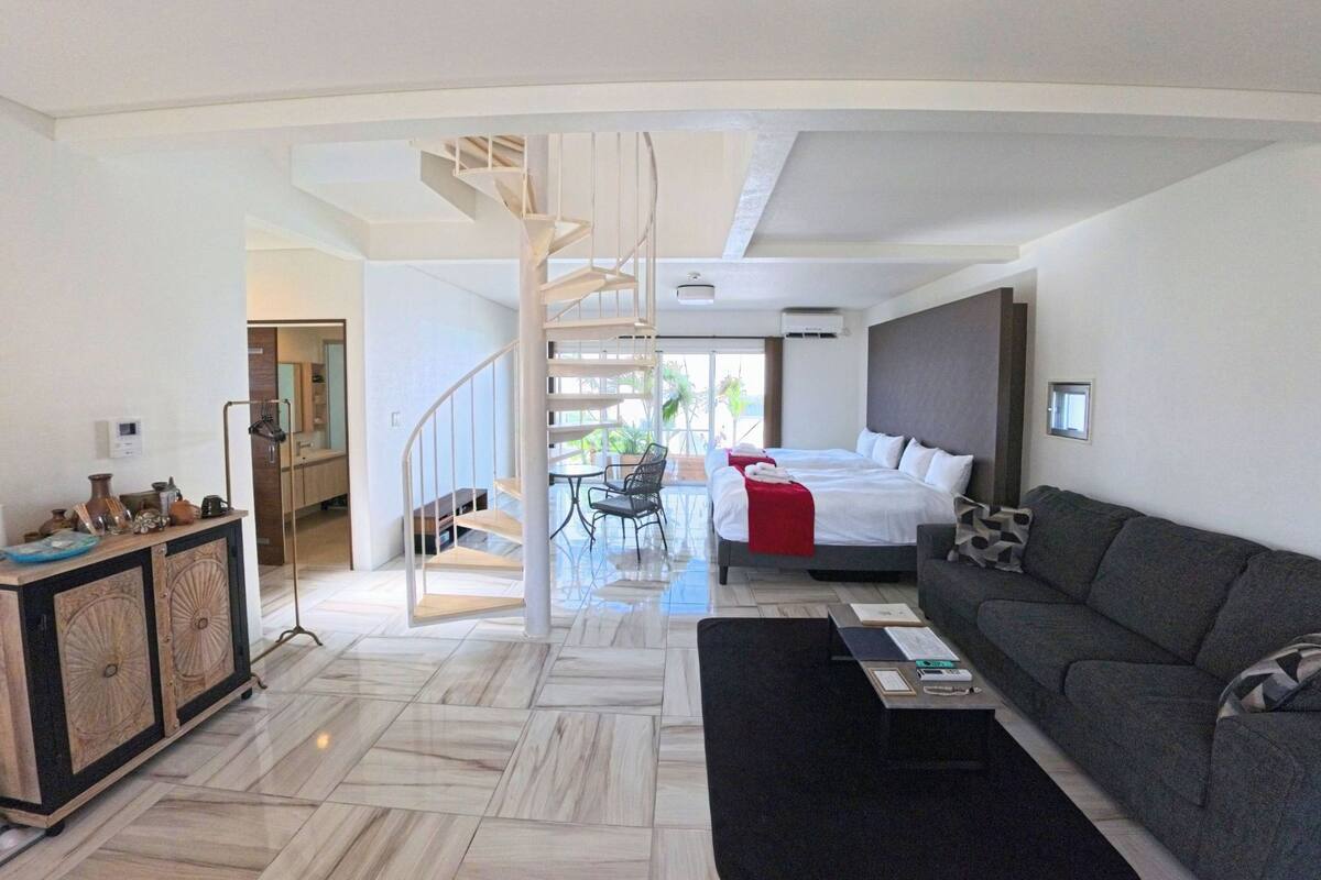 Quarto de hotel moderno com escada em espiral, cama, sofá e área de refeições.