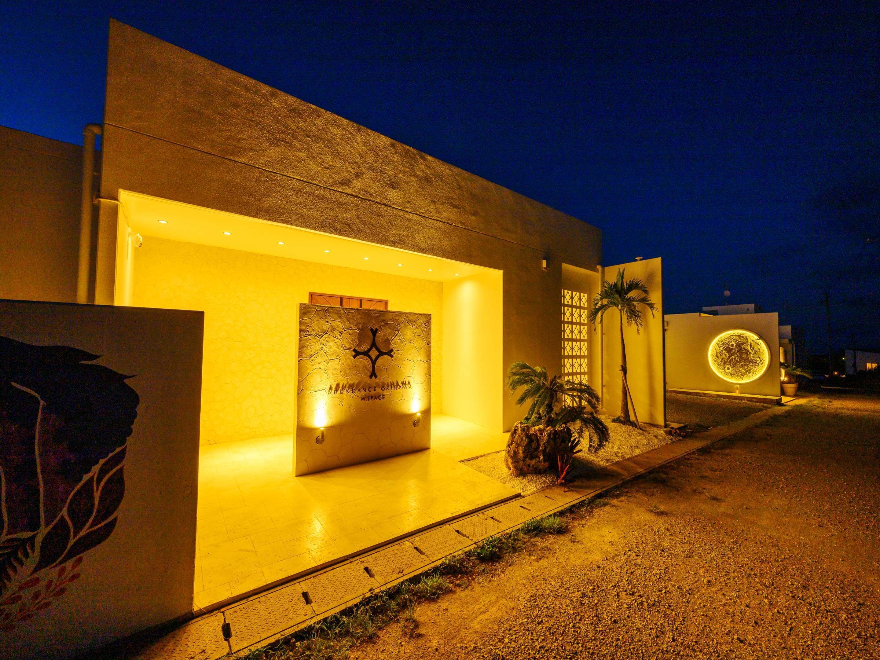 A modern building with a prominent entrance, a large illuminated sign, and palm trees.