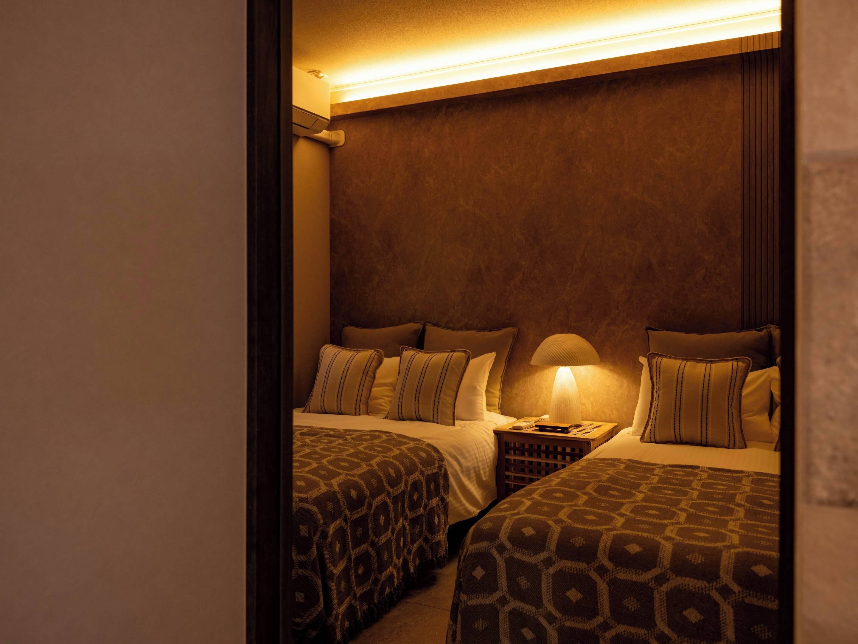 A hotel room with two beds, a nightstand, and a lamp.