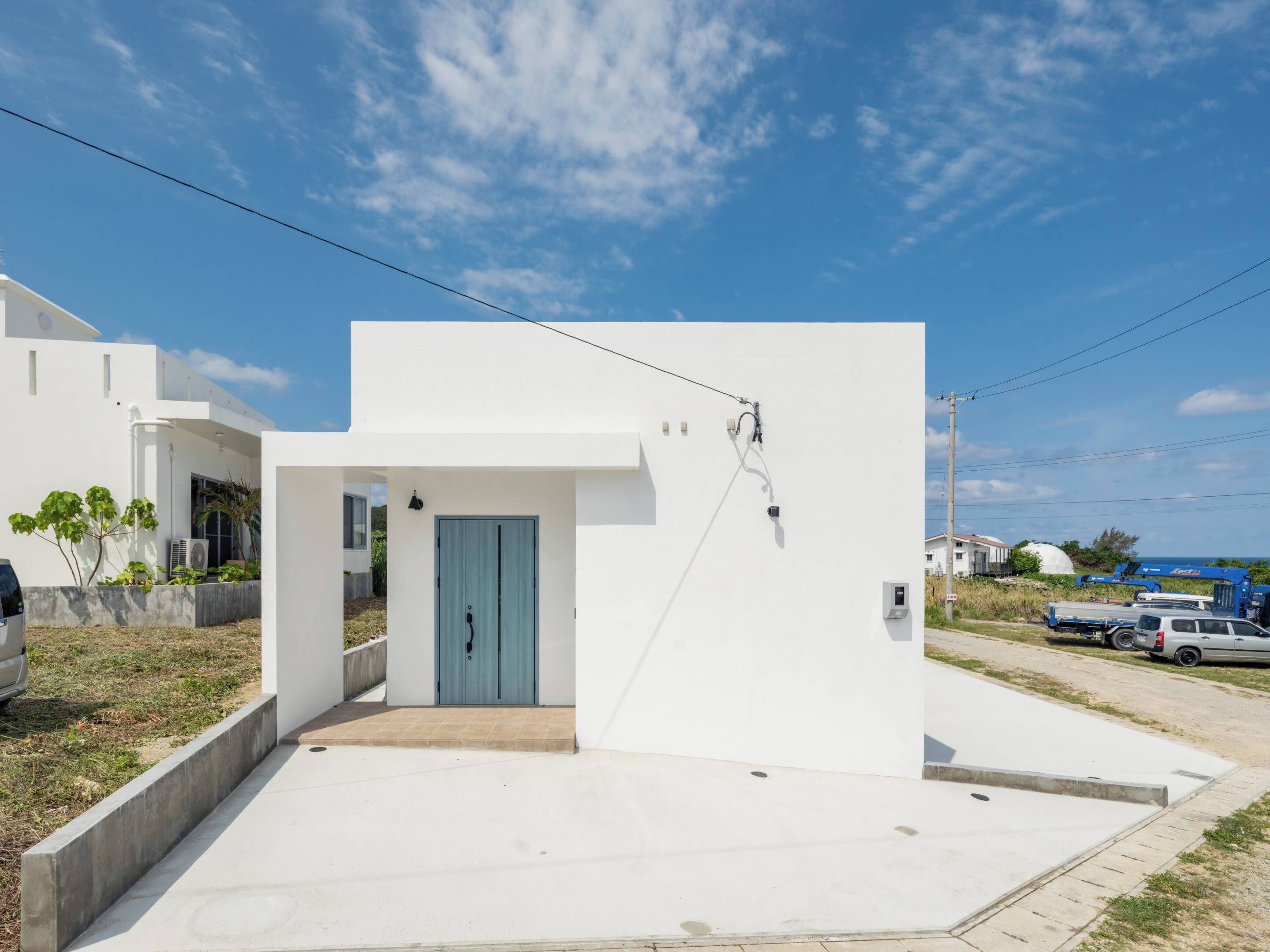 A modern white building with a blue door, a concrete entrance, and a clear sky.