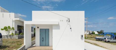 A modern white building with a blue door, a concrete entrance, and a clear sky.