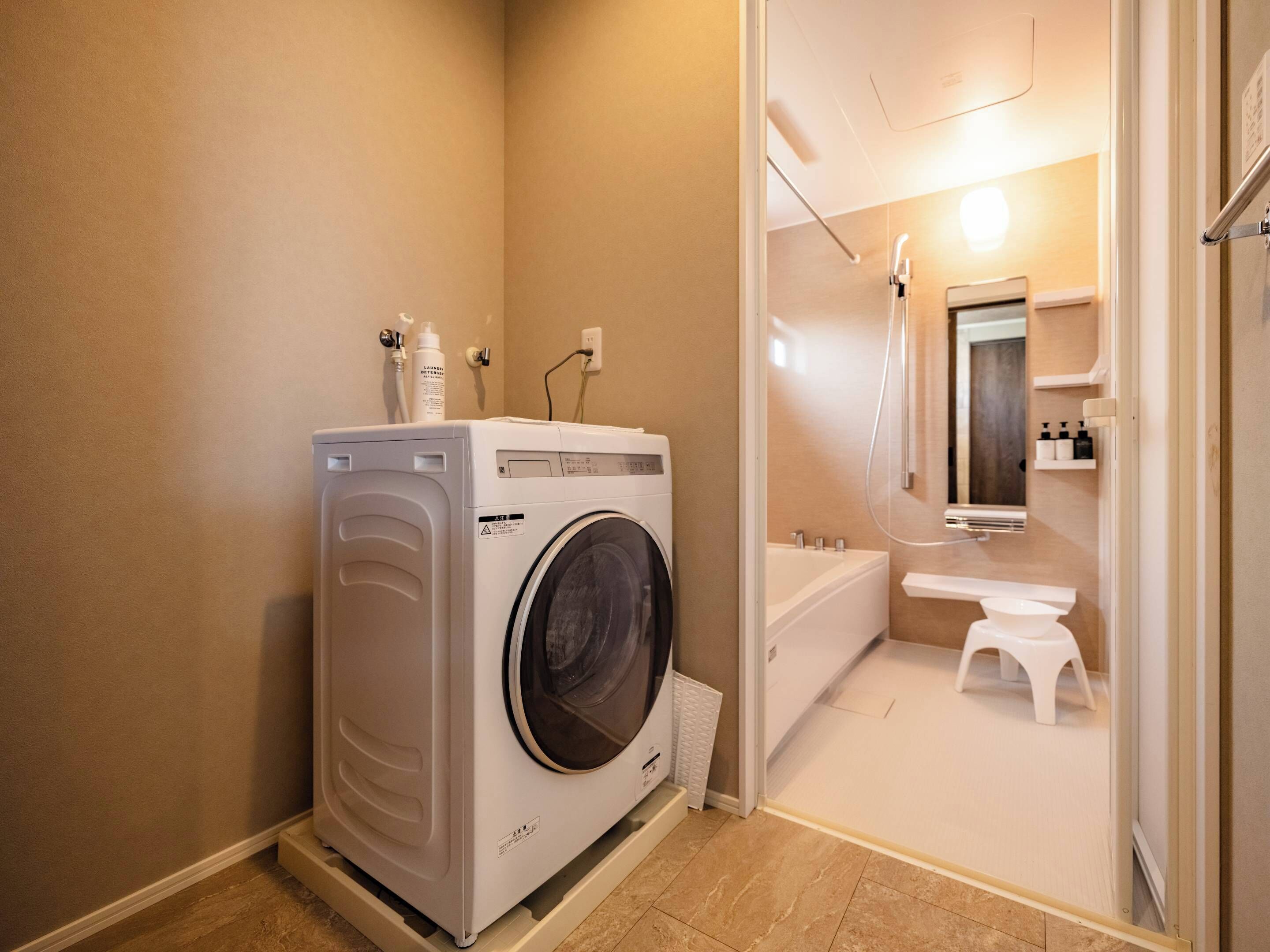 A compact bathroom with a washing machine, a bathtub, and a small stool.