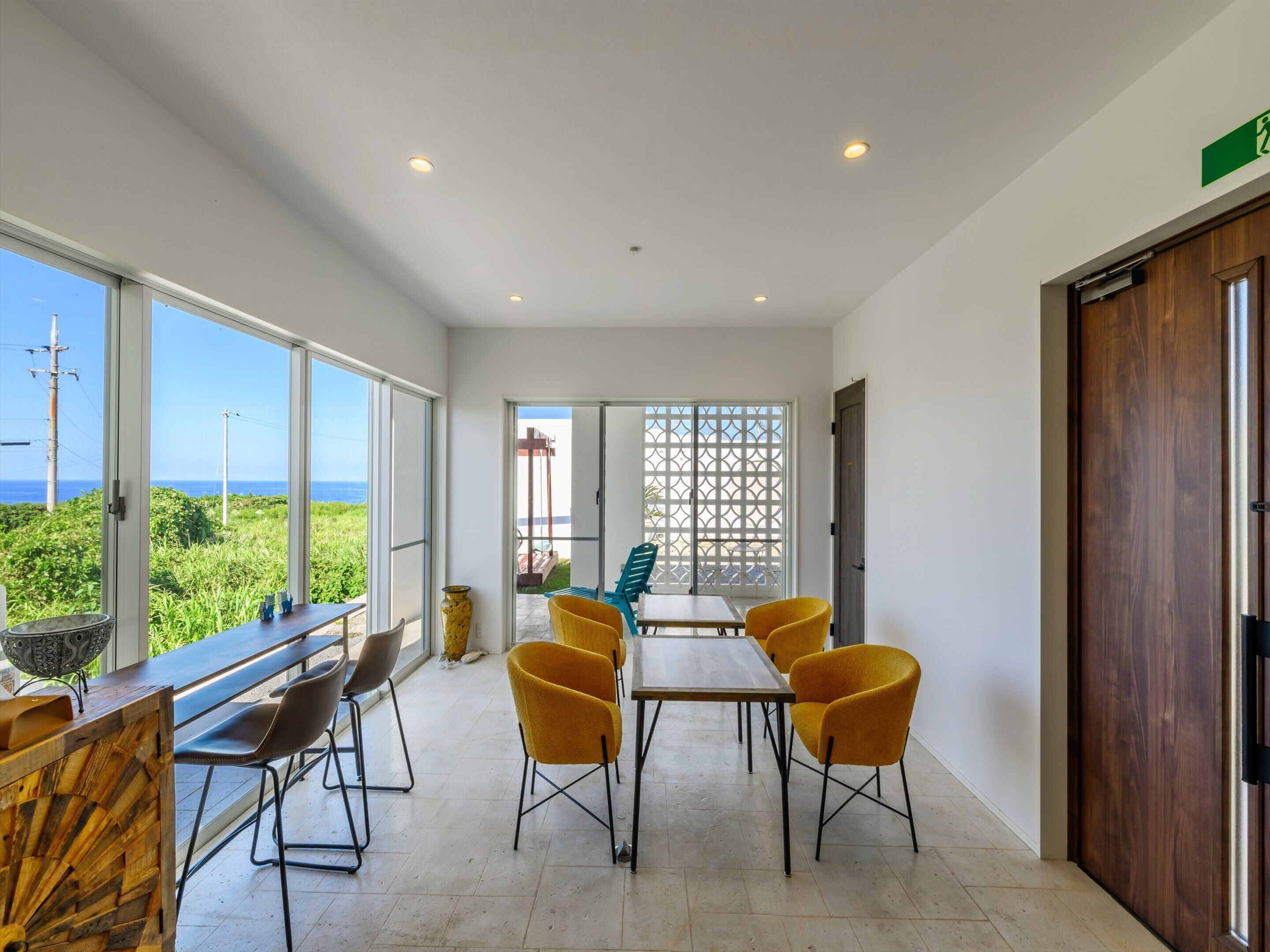 A dining area with a view of the ocean, a wooden table, and yellow chairs.