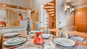 Un coin repas avec une table en bois dressée pour quatre personnes, entourée de chaises en bois. Une bouilloire rouge et des verres à vin sont posés sur la table.