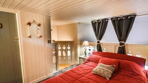 Une chambre avec une couvre-lit rouge, une table de chevet avec une lampe et une porte ornée d’un motif en forme de cœur.