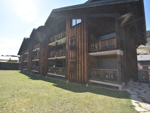 A multi-story wooden building with balconies, a grassy yard, and a paved walkway. - Charming Apartment Near Slopes and Village Center - Up to 5 Guests (Les Gets)
