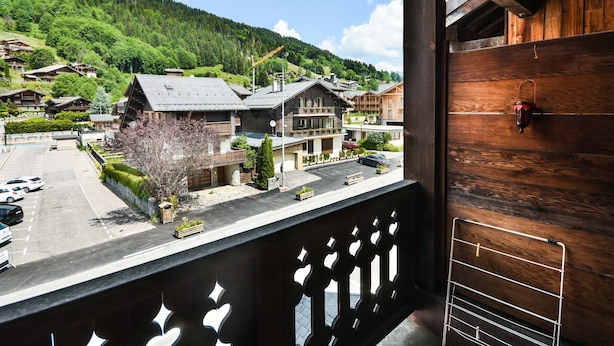 Un balcon avec vue sur une montagne et un espace de stationnement où sont garées plusieurs voitures.