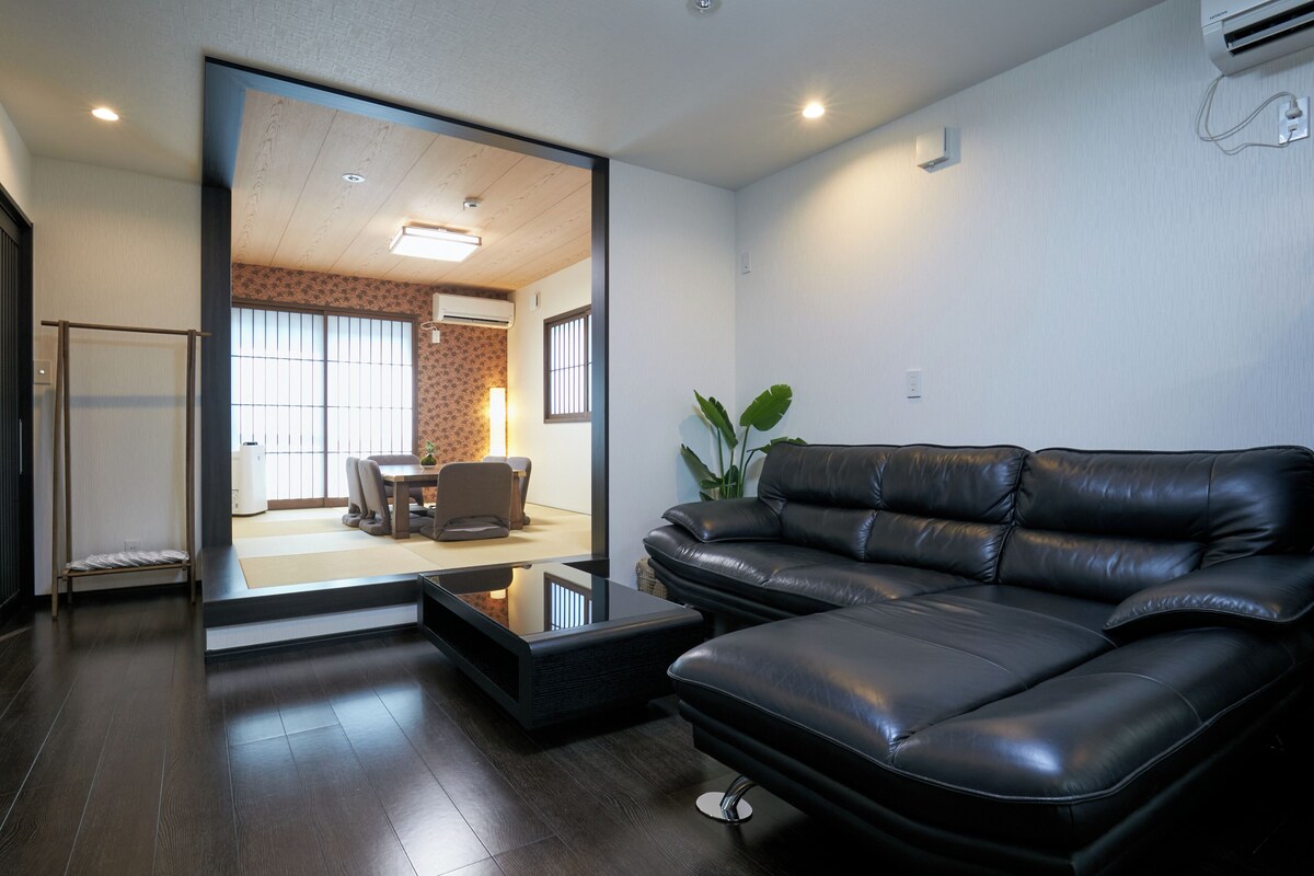A modern living room with a black leather sofa, a glass coffee table, and a tatami mat.