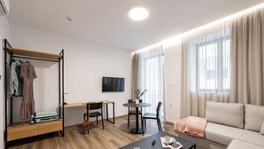 A modern, well-lit room with a sofa, a coffee table, a TV, a dining area with chairs, and a clothing rack. - Pnoe Urban Living (Nea Smirni)