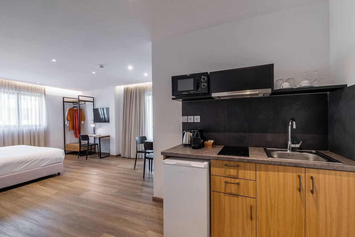 Quarto de hotel compacto com cozinha compacta, uma cama, escrivaninha e uma cadeira.