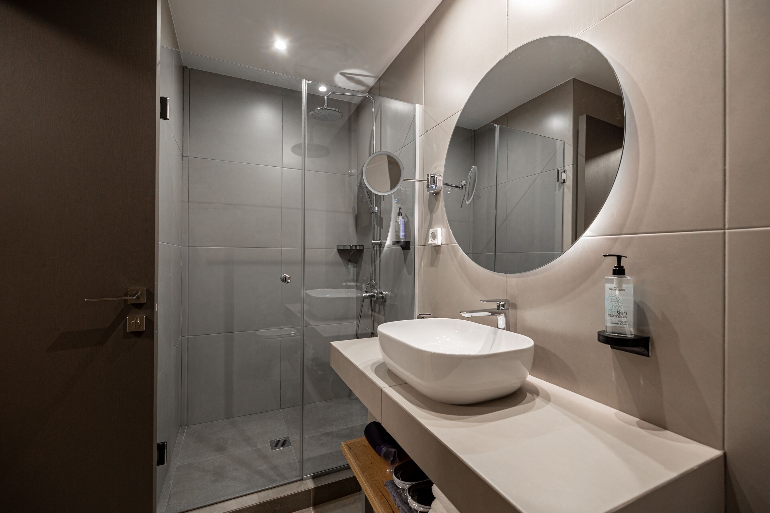 Une salle de bain moderne avec une douche à parois de verre, un grand miroir ovale et un lavabo blanc.