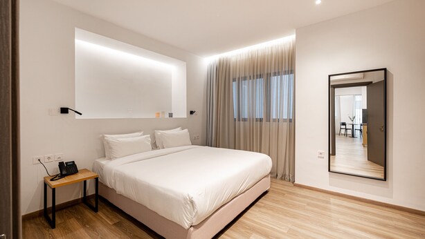 A modern bedroom with a large bed, a bedside table with a phone, and a mirror on the wall. - Pnoe Urban Living (Nea Smirni)
