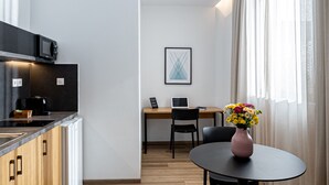 A modern kitchen with a microwave, stove, and cabinets. There is a dining area with a table, chairs, and a vase of flowers. - Pnoe Urban Living (Nea Smirni)