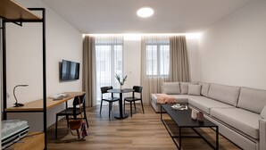 A modern living room with a sofa, a coffee table, a TV, a dining table with chairs, and a wooden desk. - Pnoe Urban Living (Nea Smirni)