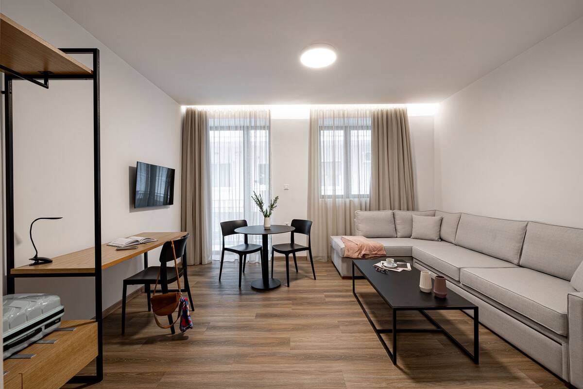 Uma sala de estar moderna com sofá, mesa de centro, televisão, mesa de jantar com cadeiras e escrivaninha de madeira.