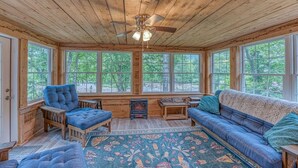 A cozy room with a wooden ceiling, large windows, a ceiling fan, a blue sofa, a blue armchair, a small table, and a patterned rug. - Riverfront House w/ Rooftop Deck! Dog Friendly! (Woodstock)