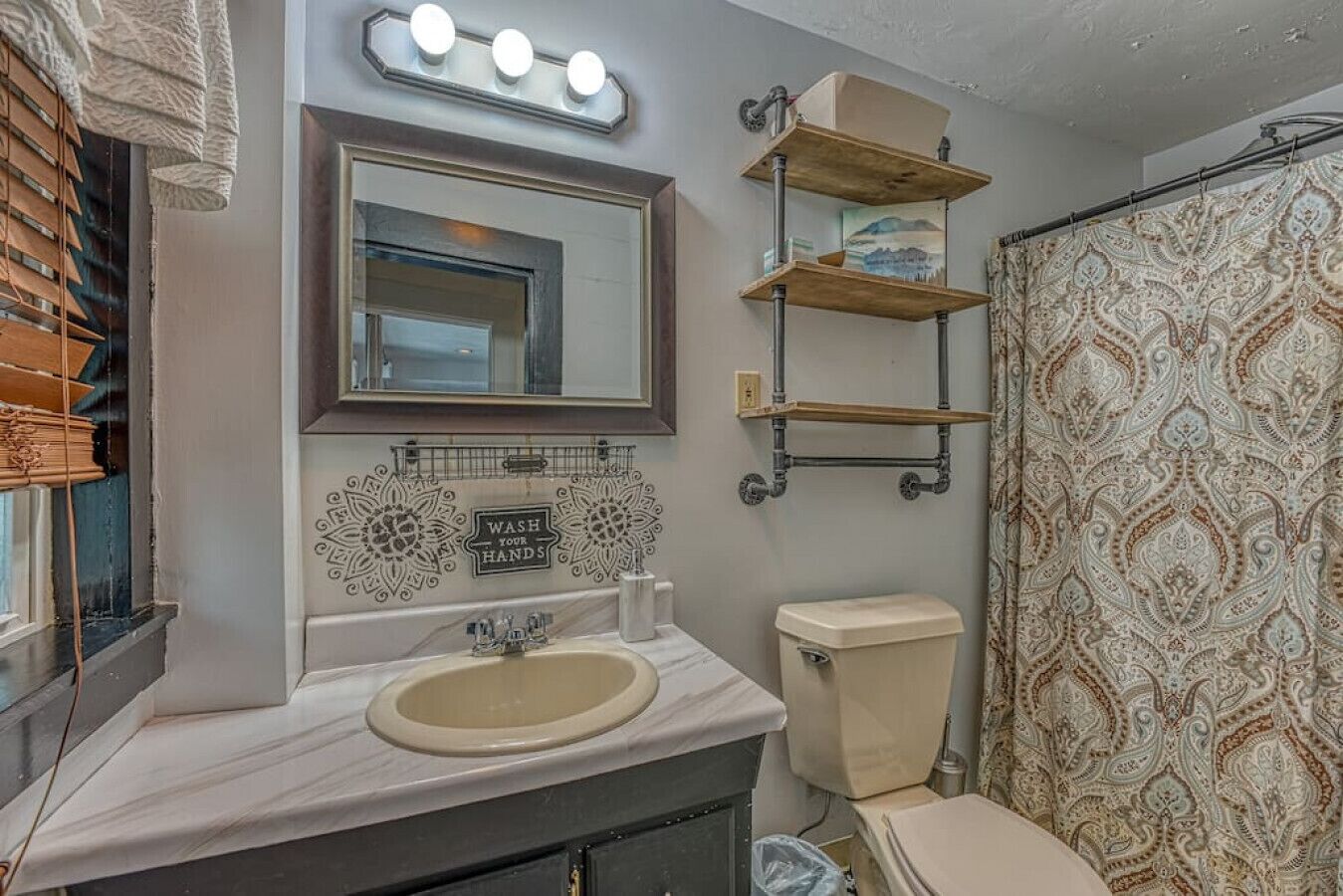 A bathroom with a sink, mirror, vanity, toilet, and shower curtain.