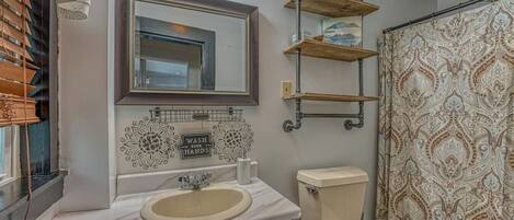 A bathroom with a sink, mirror, vanity, toilet, and shower curtain.