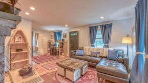 A cozy living room with a leather sofa, a coffee table, and a bookshelf. - Riverfront House w/ Rooftop Deck! Dog Friendly! (Woodstock)