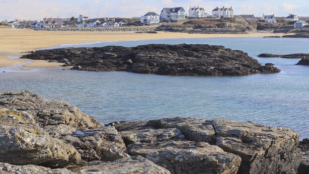 Une zone côtière caractérisée par des rivages rocheux, une plage de sable et, au loin, des maisons blanches.