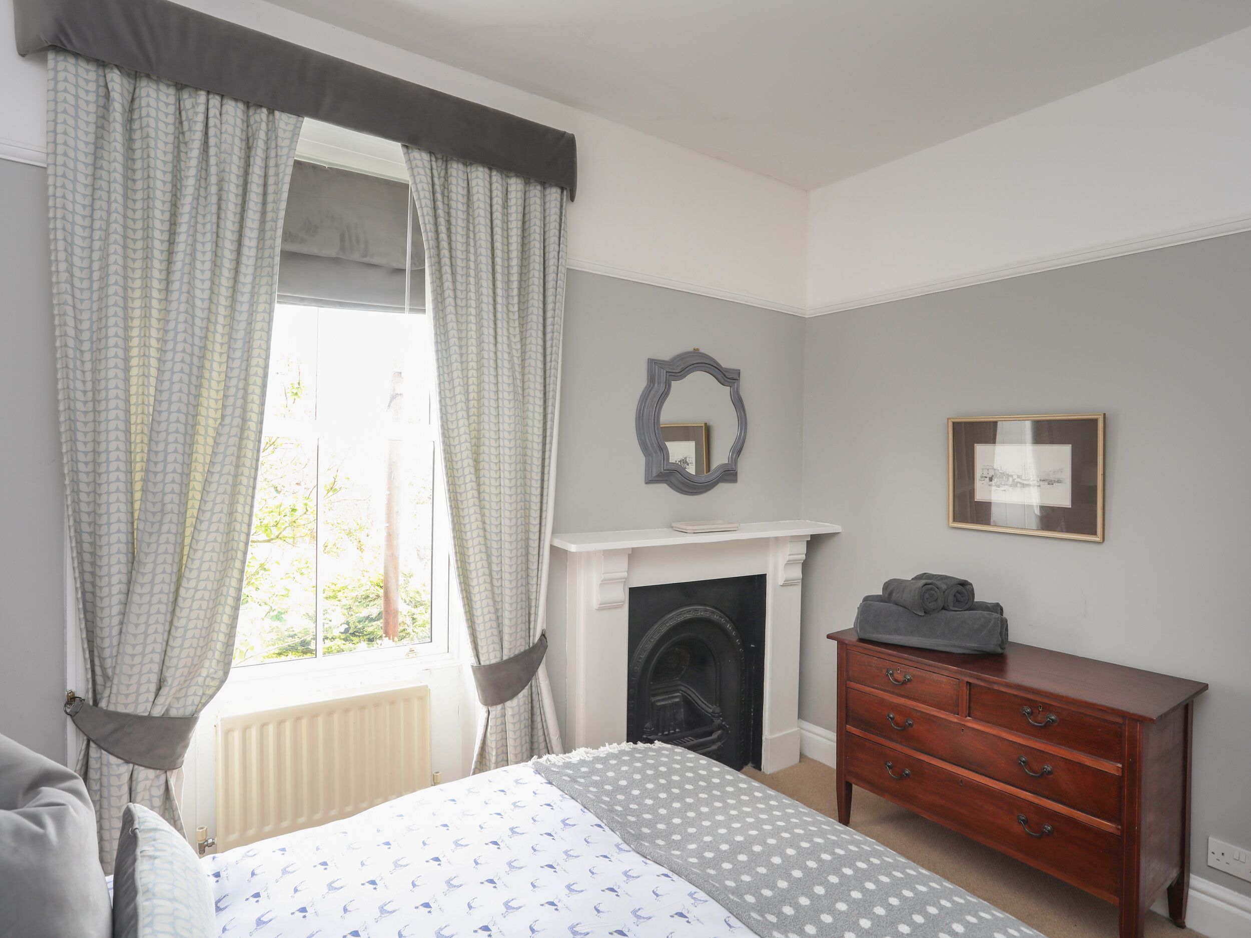 A bedroom with a bed, a dresser, a fireplace, and a window with curtains.