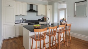 Une cuisine avec des meubles blancs, un poêle noir et un îlot central en bois doté de chaises.