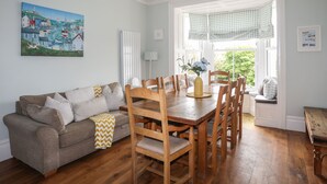 Un coin repas avec une table et des chaises en bois, un canapé avec des coussins, un radiateur et une fenêtre ornée de rideaux à carreaux.