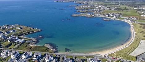 An aerial view of a coastal residential area with houses, a beach, and a clear blue sea.