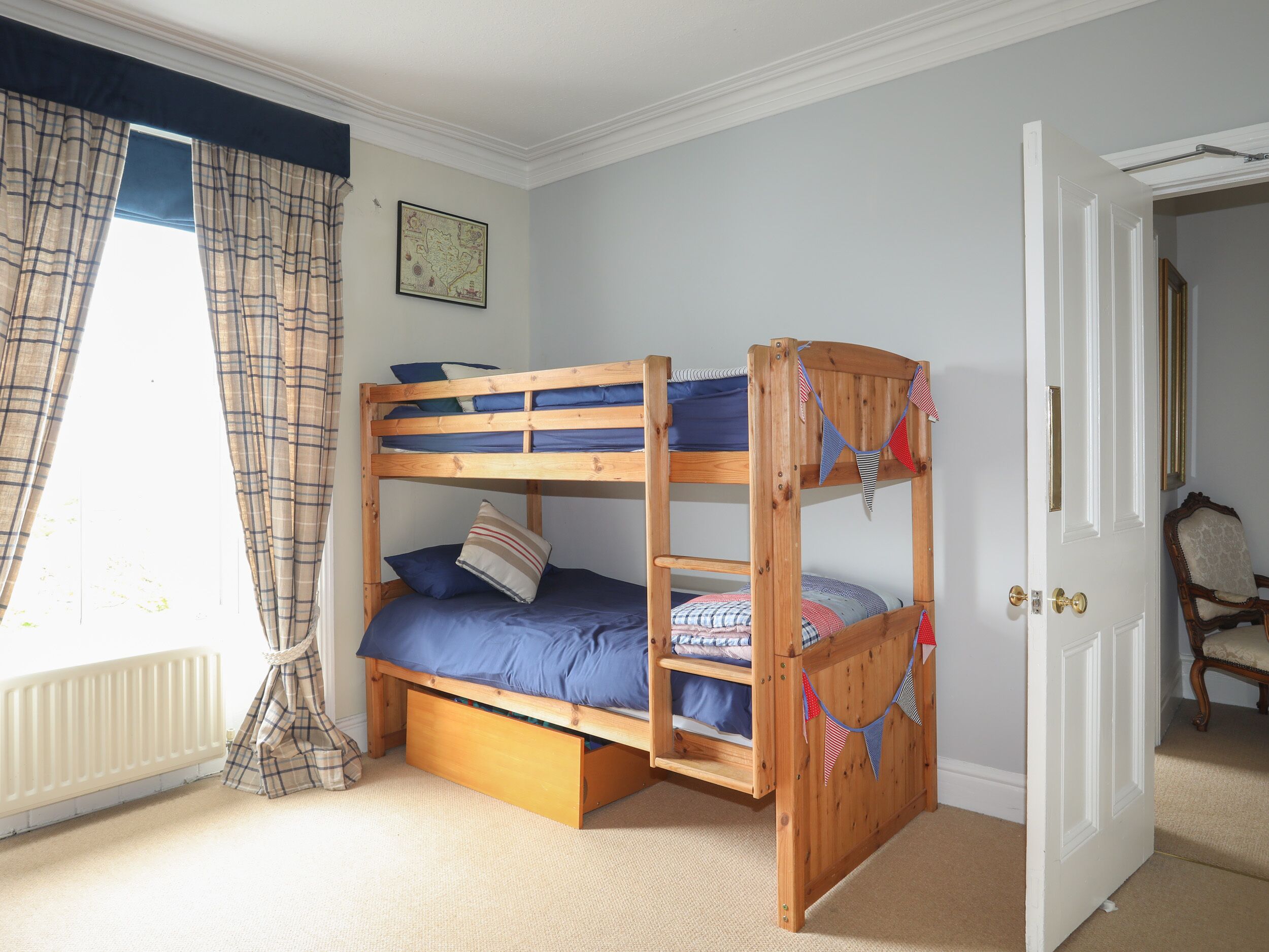A bunk bed room with a window, curtains, a radiator, and a door.