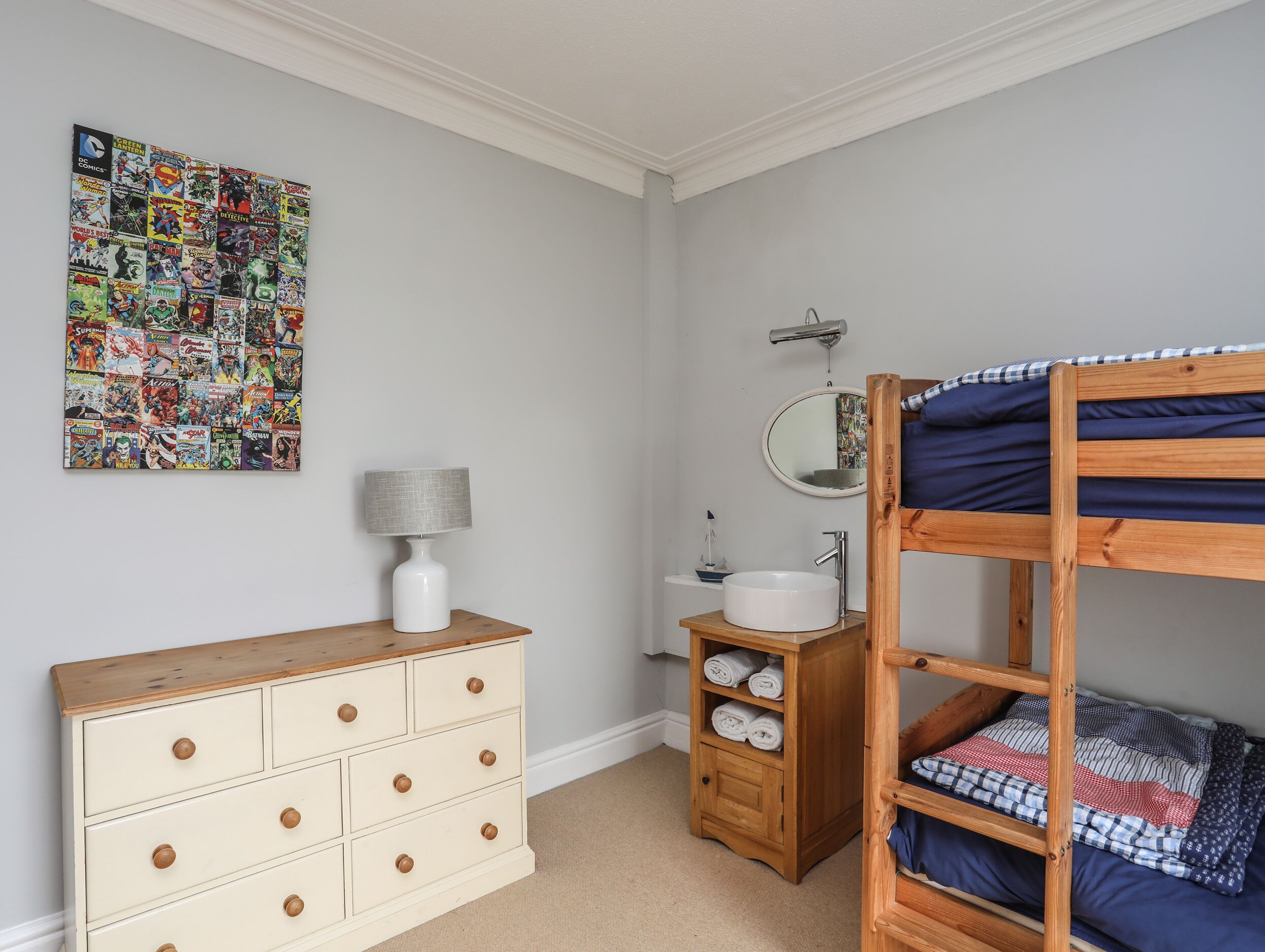 Une chambre avec un lit superposé, une commode, un miroir et une œuvre d’art murale.