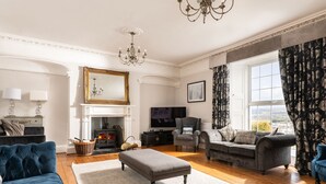 A spacious living room with a fireplace, comfortable seating, and a large window offering a view. - Fron Dderw (Bala)