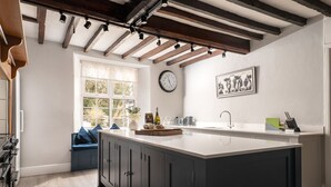 A modern kitchen with a large island, dark cabinets, and a window with a view of trees. - Fron Dderw (Bala)