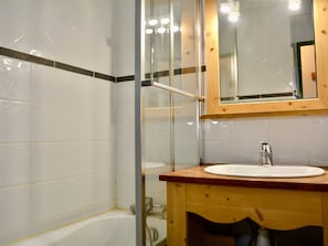 A bathroom with a white bathtub, a wooden vanity with a sink, and a mirror above the sink.